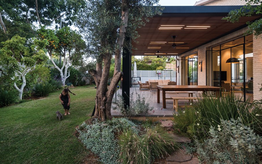 רחבת הישיבה ביציאה מחדר המגורים: הפרגולה משלבת קונסטרוקציית ברזל שחורה, שנצבעה בטכנולוגיה של צביעת מכוניות, וקורות עץ ארז, שביניהן משתלבת תאורת לד. צילום: גלעד רדט