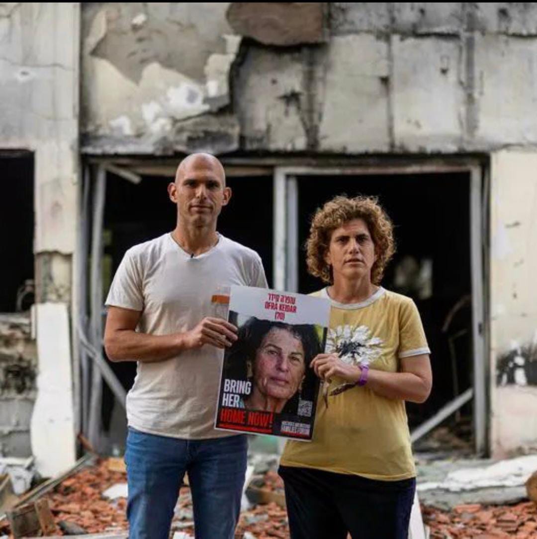 יעל ואלעד קידר, שניים מילדיה של עפרה קידר ז"ל, על רקע ביתה השרוף. קרדיט: דוברות קיבוץ בארי